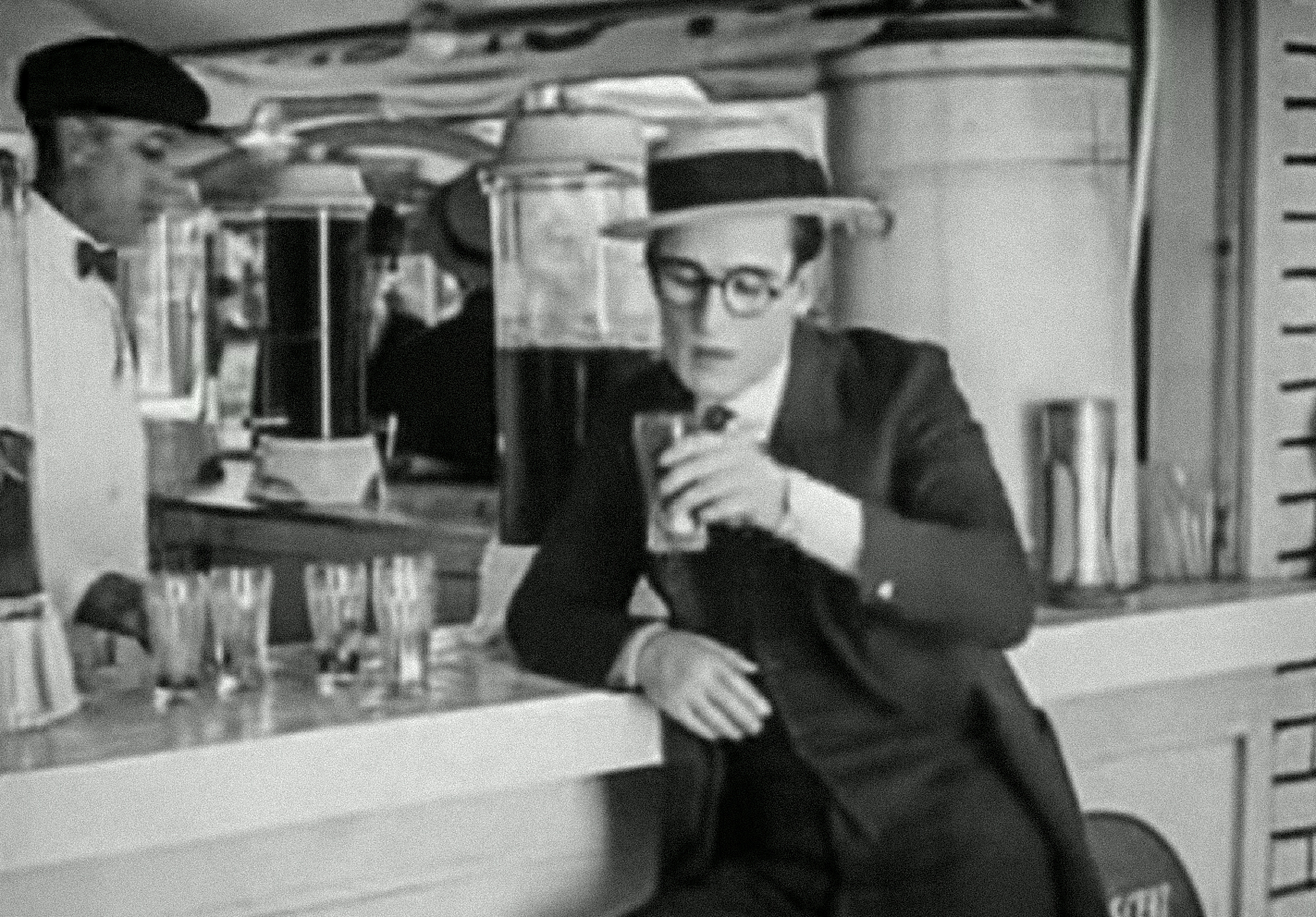 Screenshot B&W - Harold Lloyd wearing black suit and grey hat, holding a glass - from Number Please (1920)