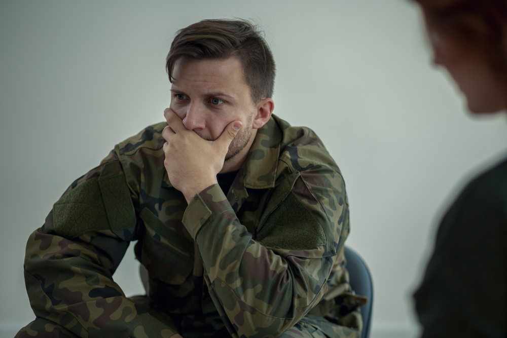 Terrified soldier in green uniform with his hand over his mouth, during a meeting with psychotherapist,