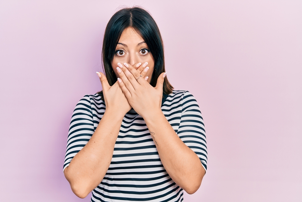 Young Hispanic woman wearing casual clothes shocked covering mouth with hands for keeping a secret