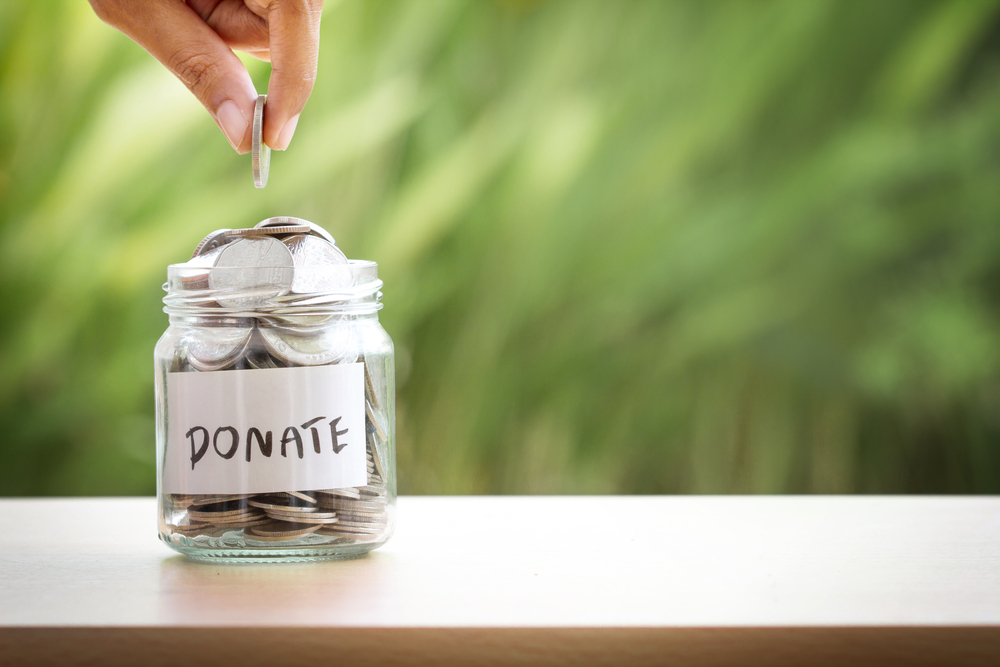 Hand putting Coins in glass jar to donate