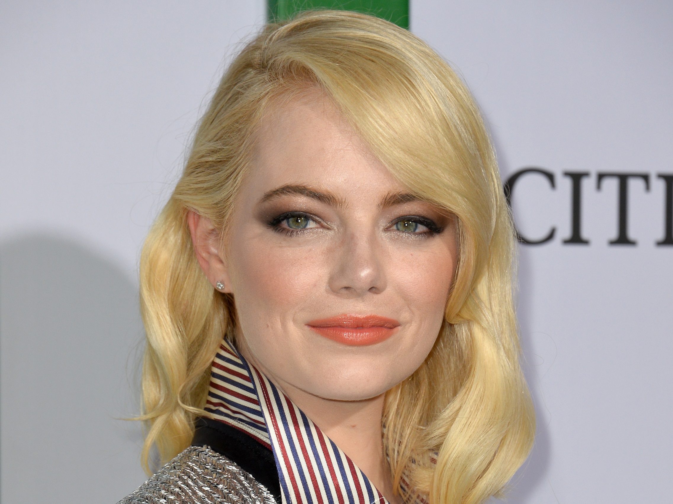 Photo of Emma Stone with blonde hair wearing shirt smiling and looking to a camera - 2017.
