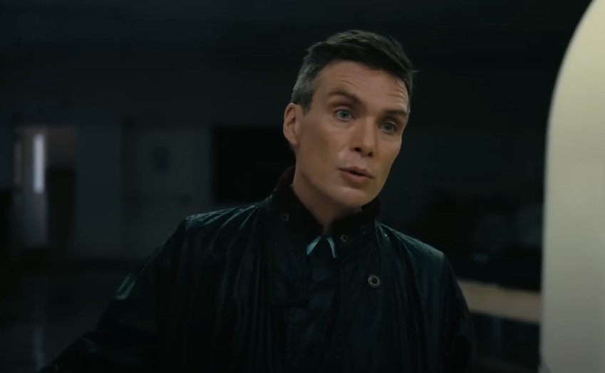 Cillian Murphy as Robert Oppenheimer in dark clothes speaking to someone