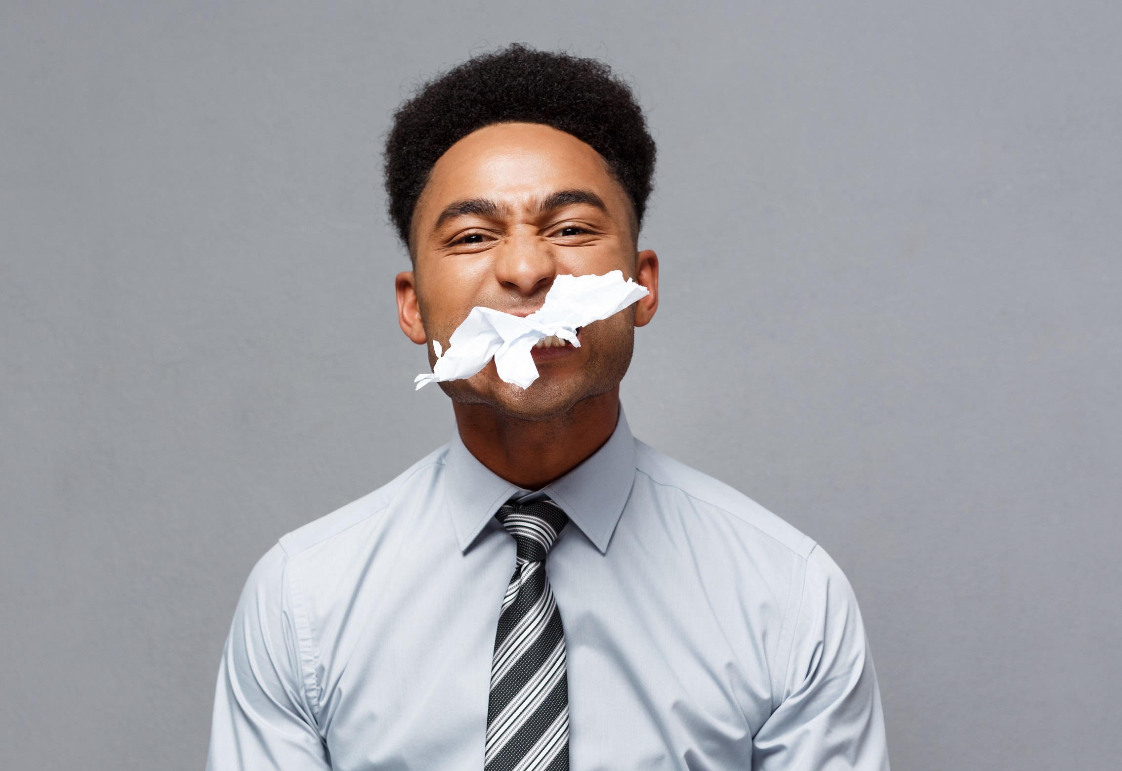 Black man eating paper ,looking to camera on grey background.