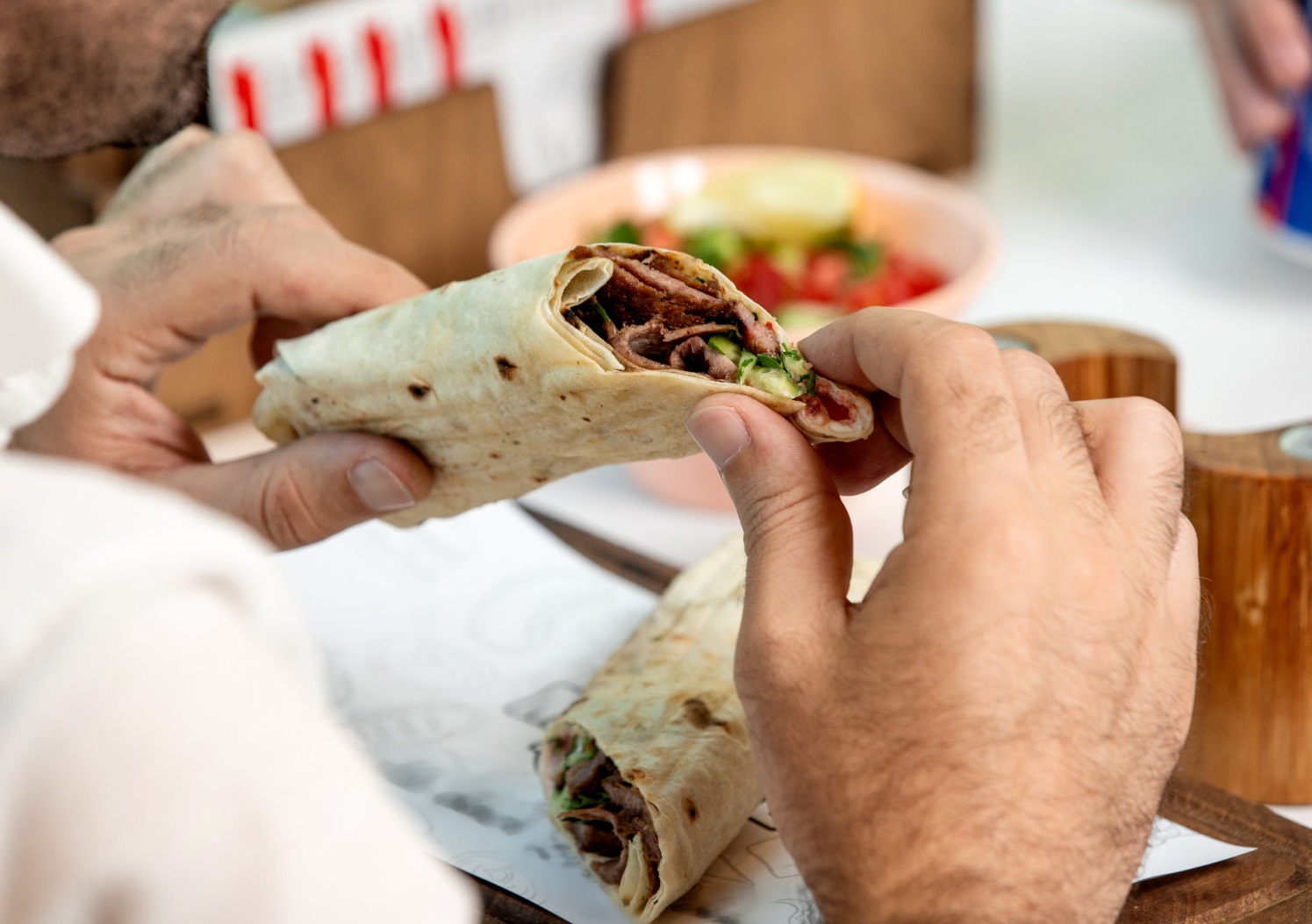 Man holding beef burger wrapped in flatbread.