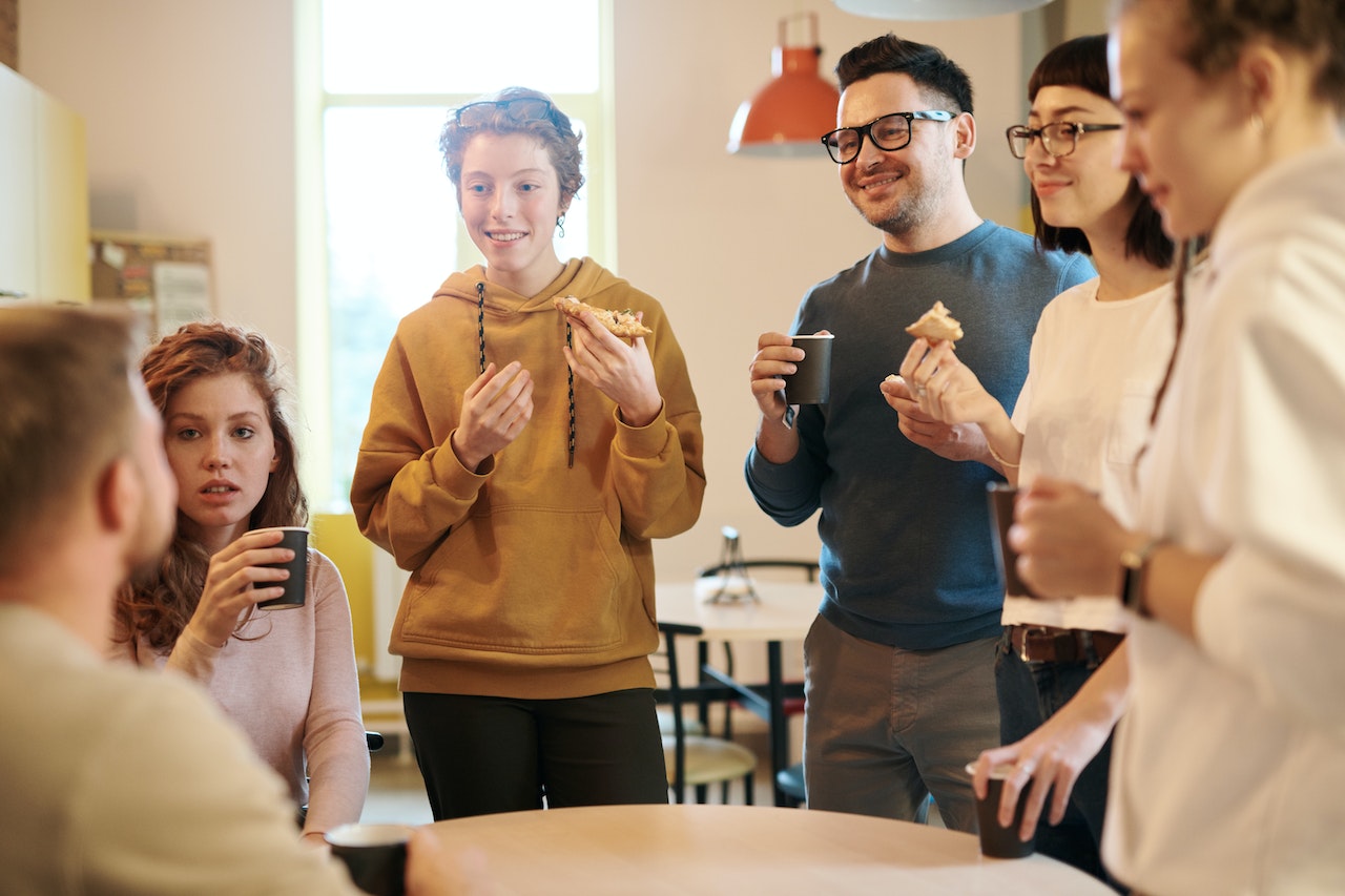 Men and women standing beside table having lunch.