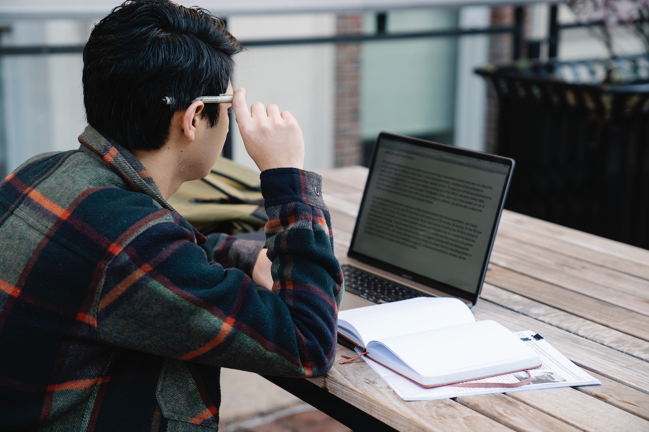 Photo of a man wearing dark shirt reading on his laptop.