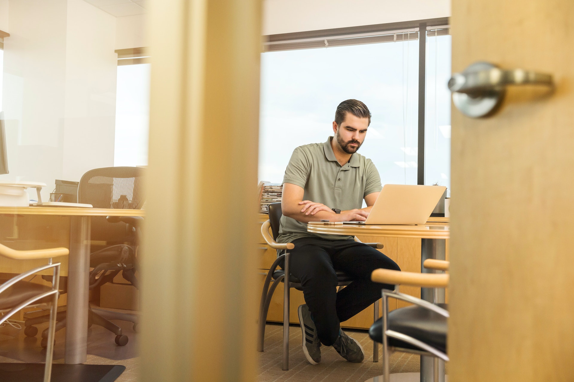 Man working on laptop sitting at his desk in office in green shirt