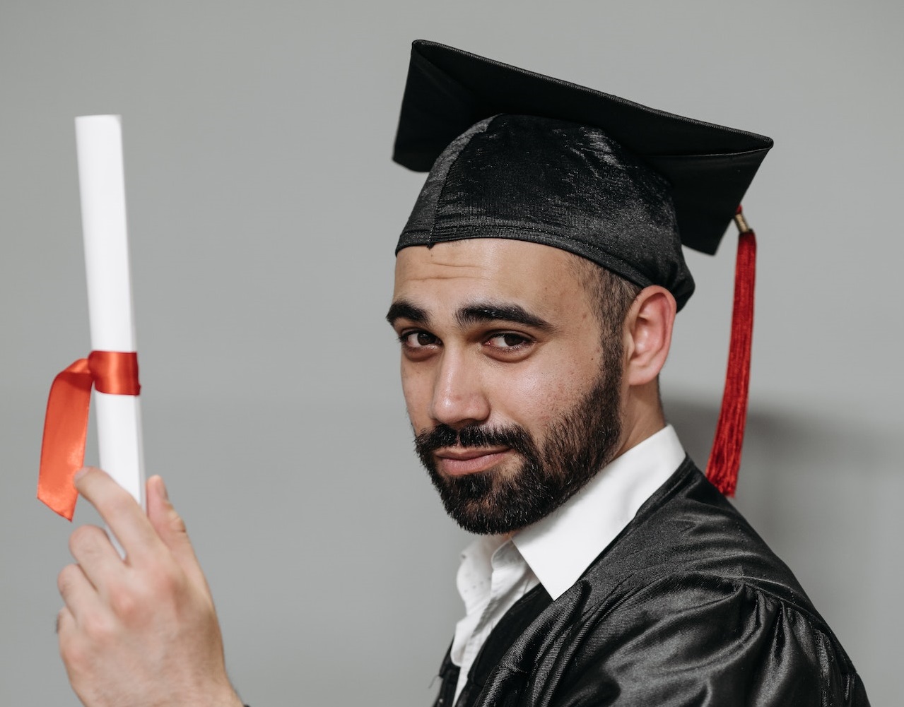 Man wearing black graduation uniform and hat is holding a diploma.