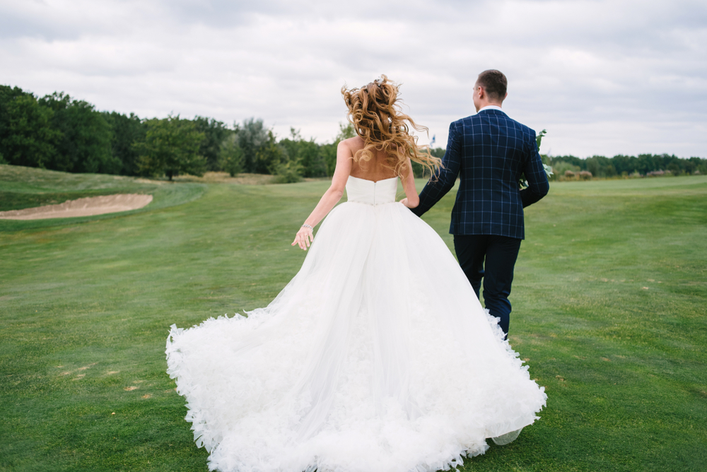 Bride and groom running on green grass of golf course