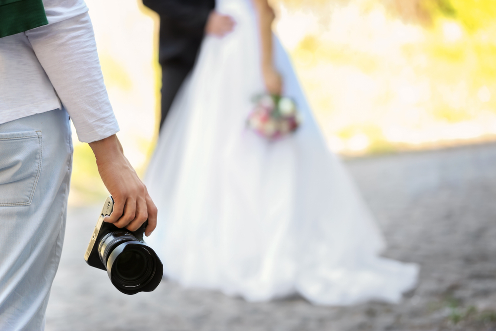 Professional photographer with camera and wedding couple