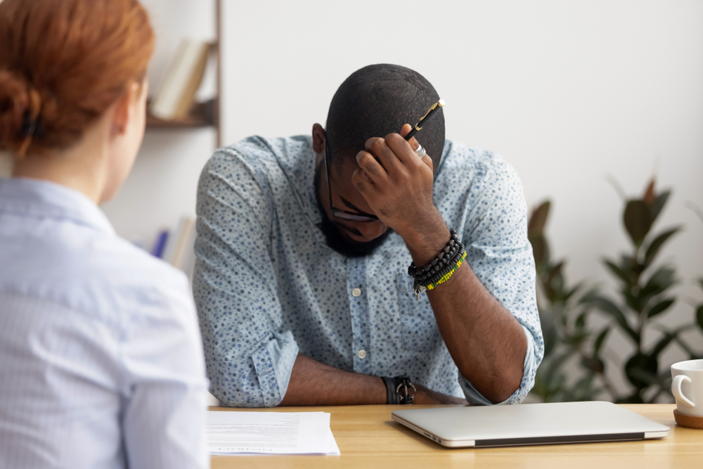 Stressed upset employee in blue shirt sitting at a table disappointed