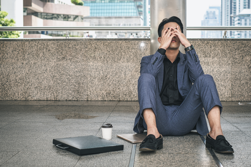 Shocked employee in a suit sitting outside with hands on his head after being fired