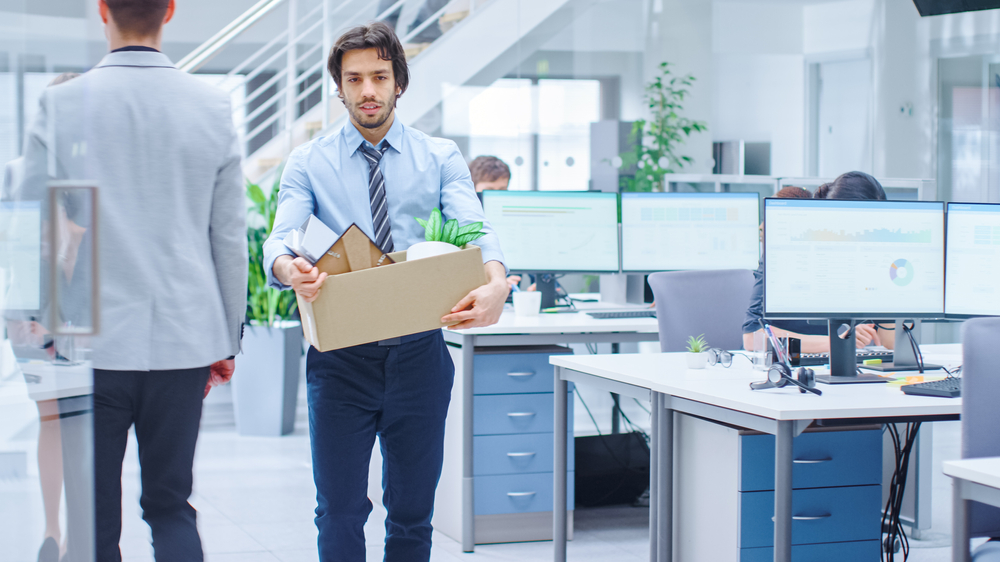 Sad Fired / Let Go Office Worker in suit Packs His Belongings into Cardboard Box