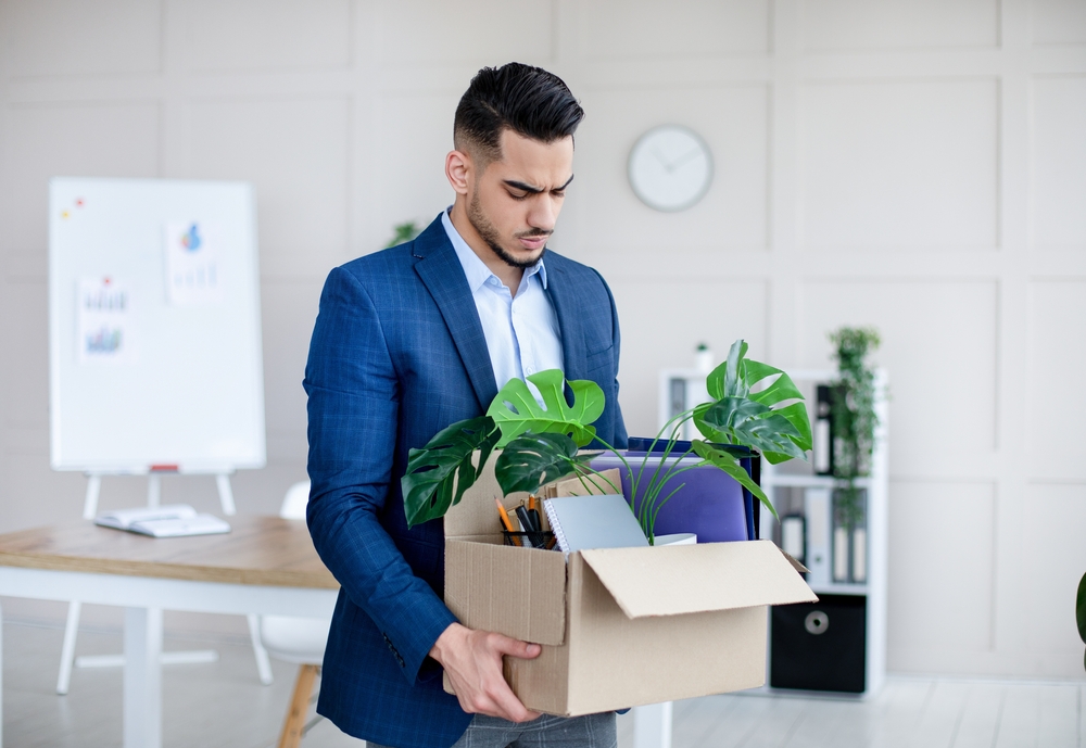 Unemployed guy in formal wear holding personal belongings, feeling depressed after losing his job