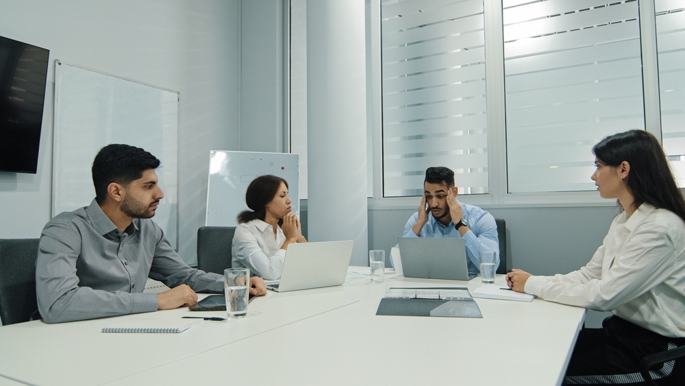 Shocked employee in blue shirt sitting at a meeting being fired on the spot