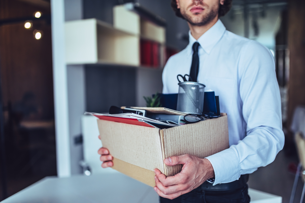Young handsome businessman in suit  in light modern office with carton box collecting his stuff after being fired