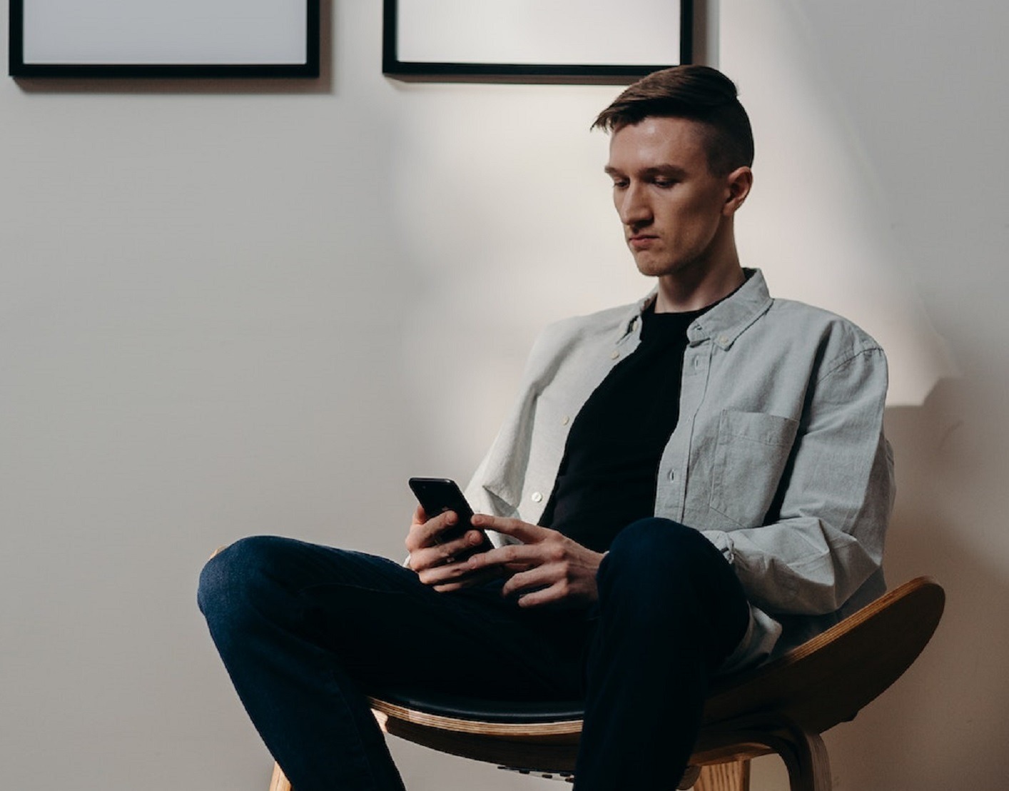 Sad man wearing black t-shirt and grey shirt seating on the chair looking at phone.