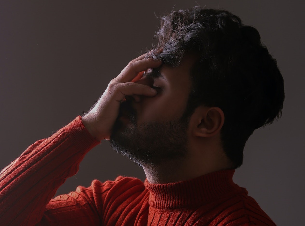 Disappointed man wearing red sweater covering his face.