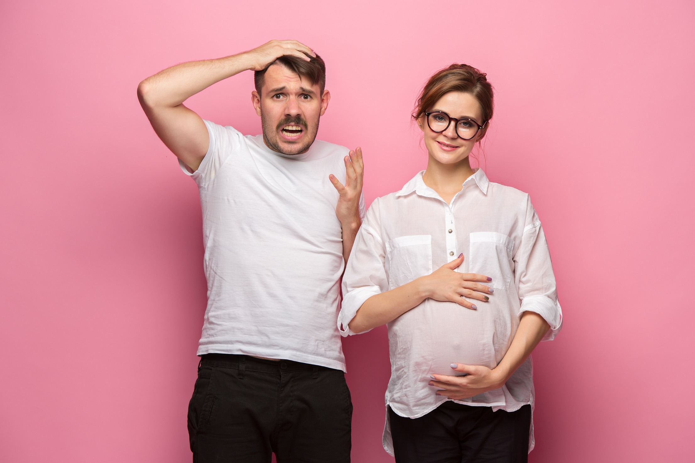 Surprised man standing by pregnant woman on the pink background.