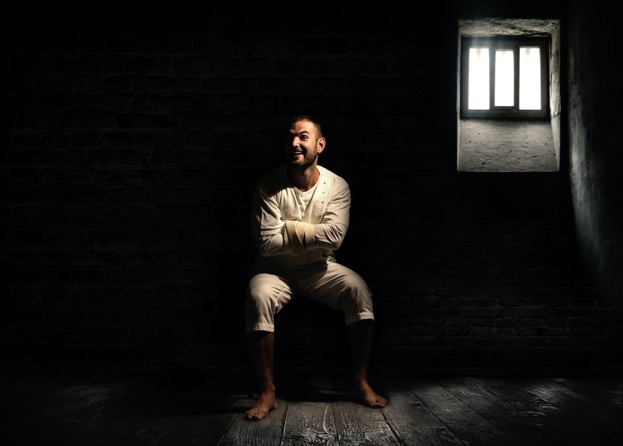 A crazy man wearing white clothes sitting inside a dark hospital room.