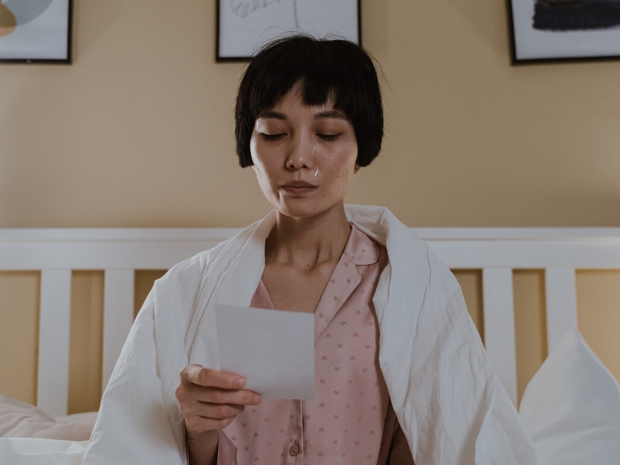 Woman wearing pink pajamas reading letter ,seating on the bed.