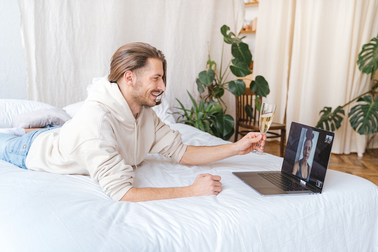 Man with long laying on the bed and having a video call.
