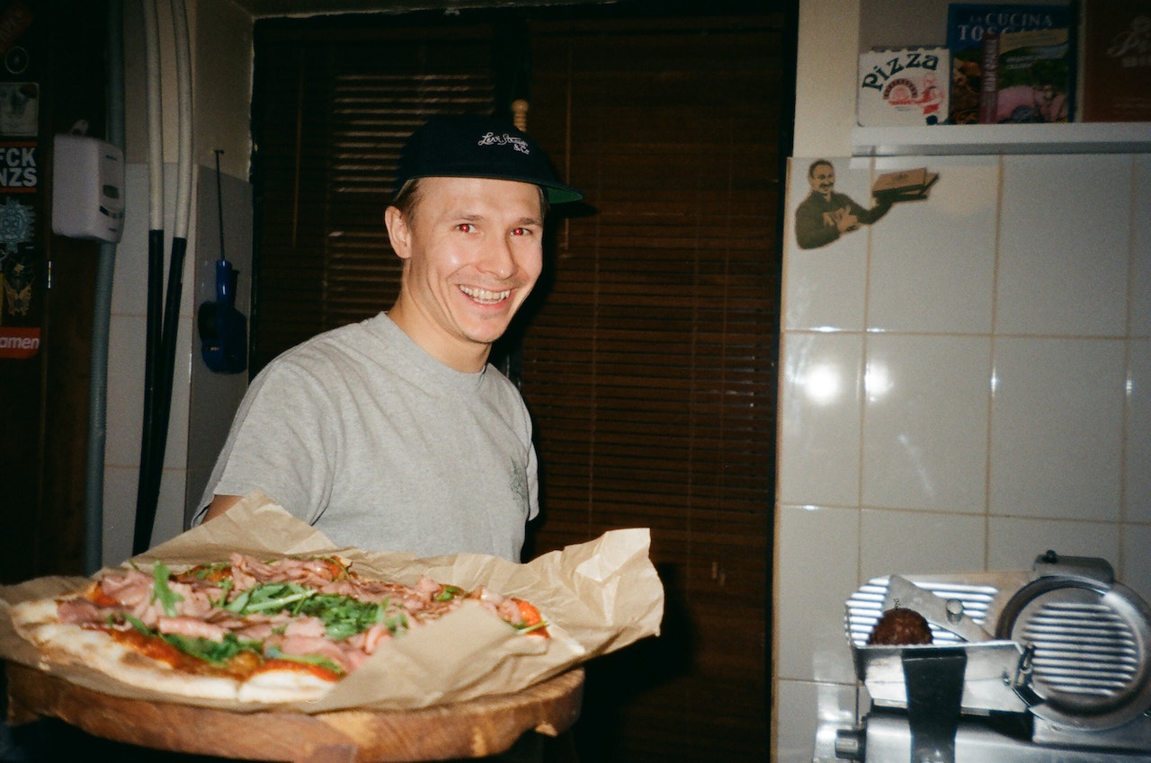 Man is holding a hot pizza and smiling.