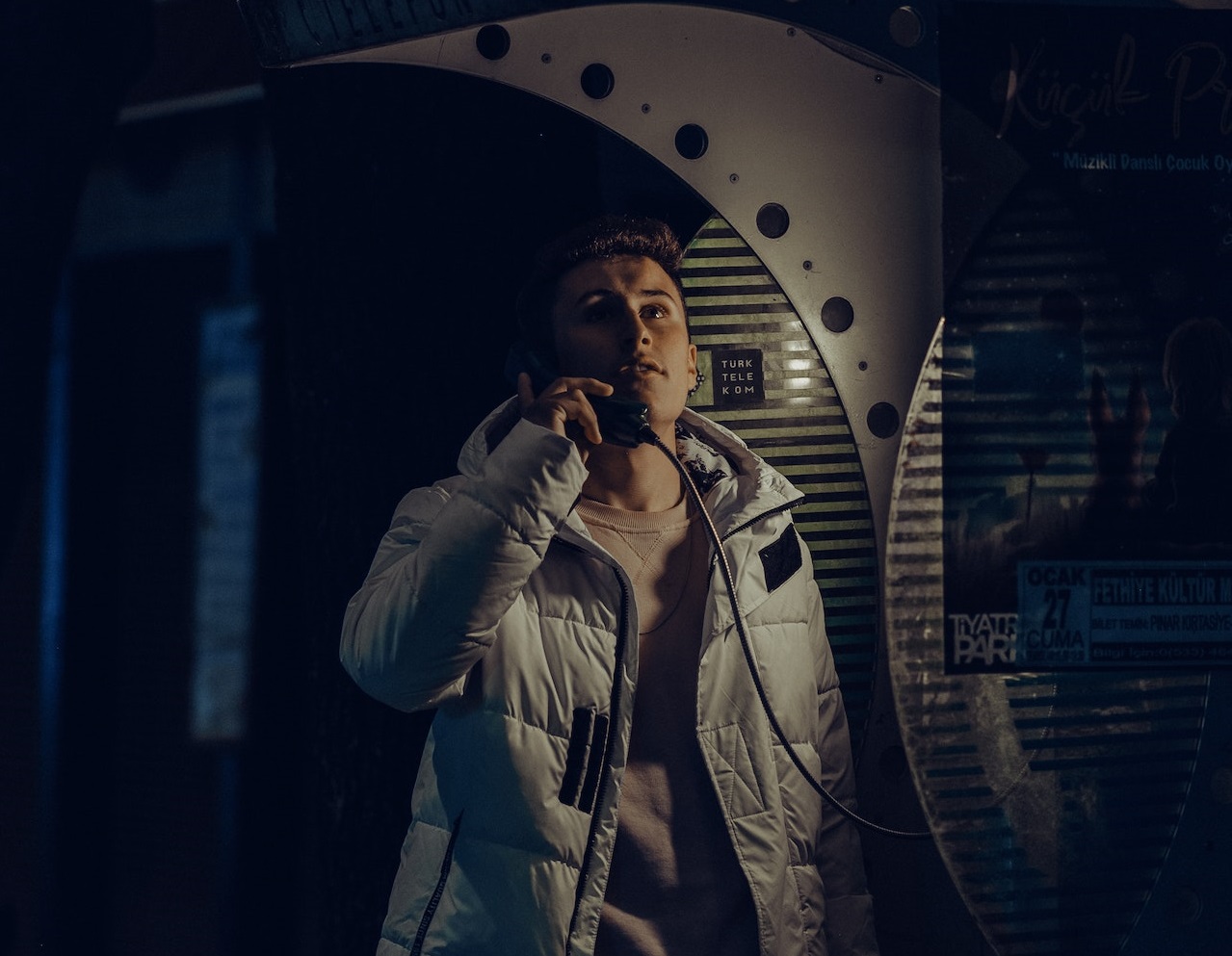 Man wearing grey jacket is talking on the pay phone.