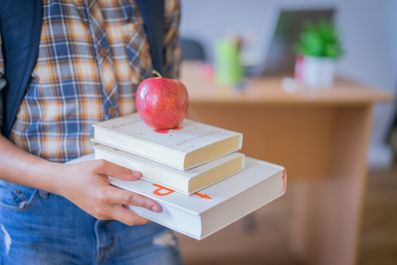 Kid holding a books and red apple.