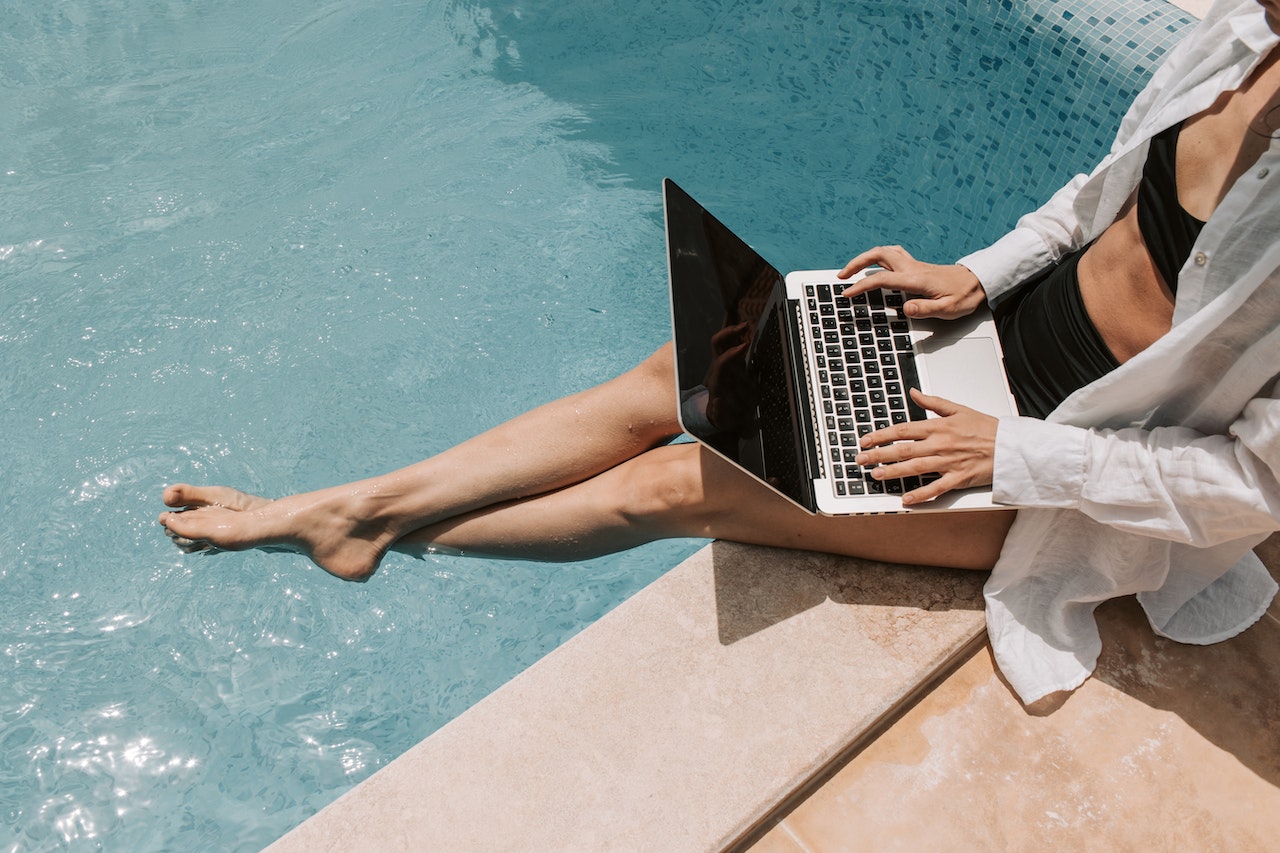 Woman sitting on poolside using laptop.