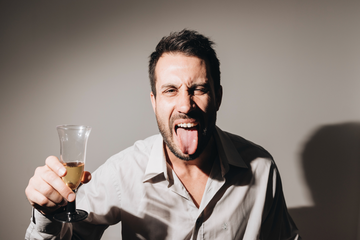 Man with tongue out ,holding a glass and looking at camera.