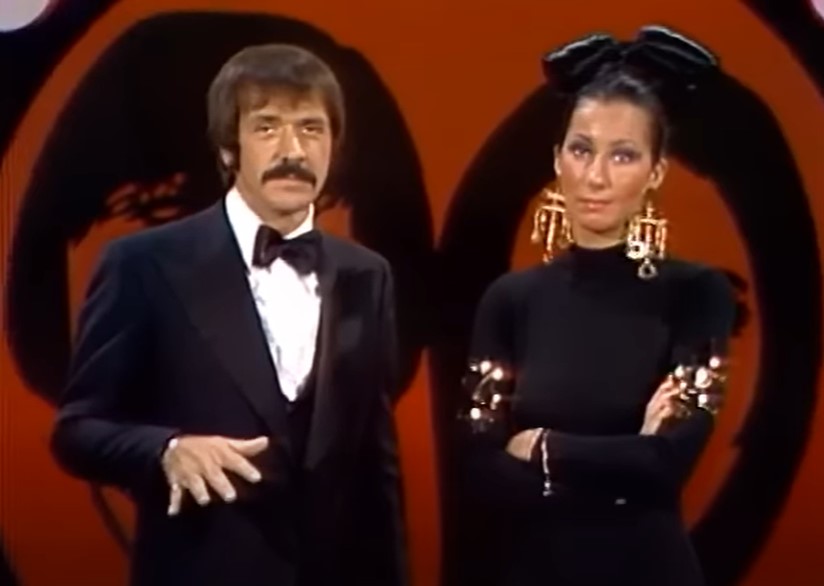 Sonny & Cher on stage in black formal clothes looking displeased