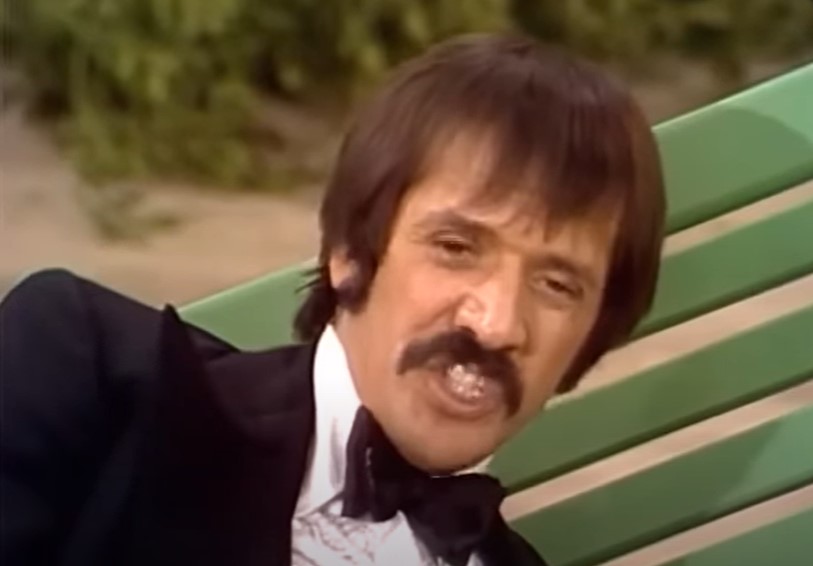 Sonny Bono in The Sonny and Cher Comedy Hour in suit sitting on a green bench