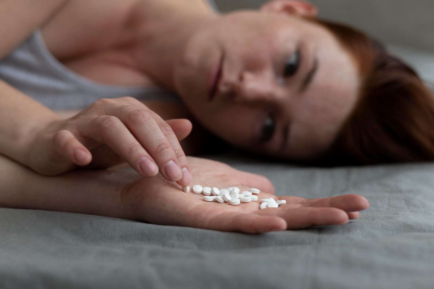 Depressed woman holding pills and laying on the bed.