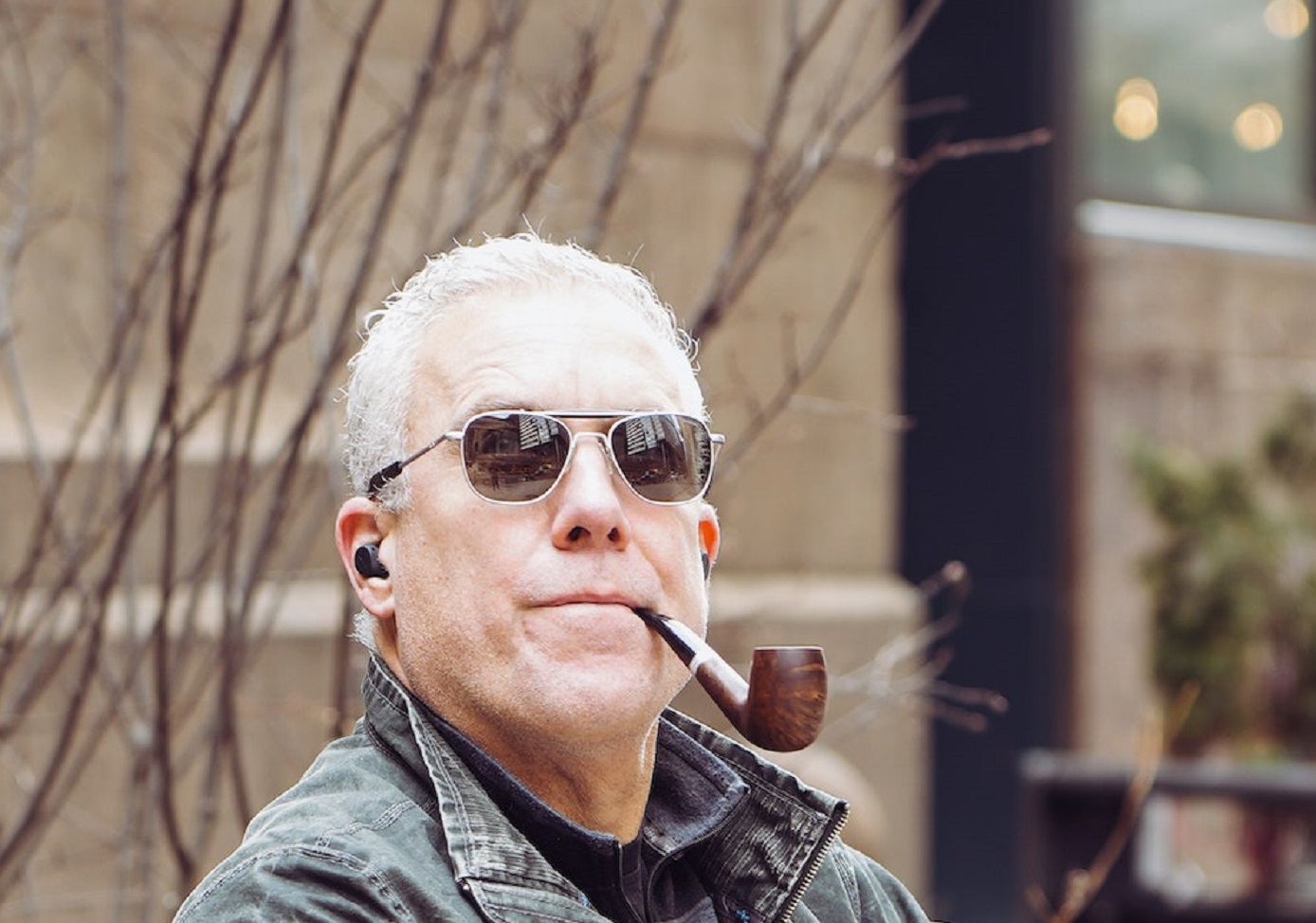 An elderly man with sunglasses and tobacco pipe sitting outside.