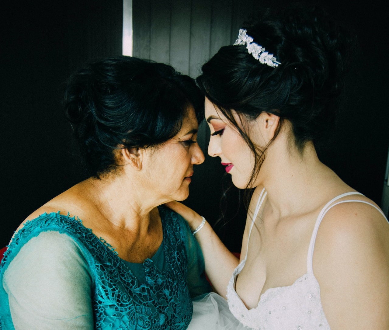 Woman is standing next to a bride wearing white dress an looking at her eyes.