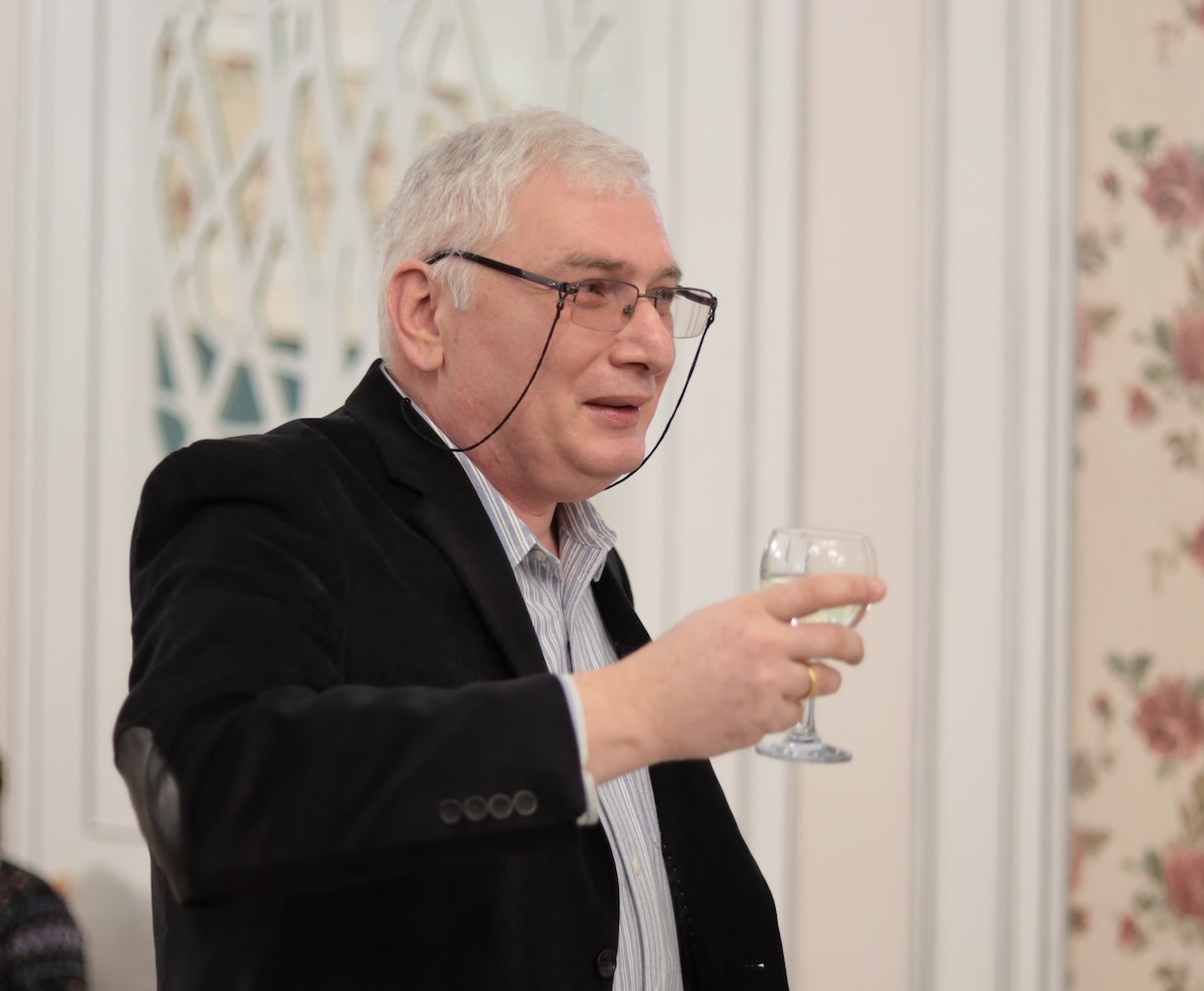 An elderly man is holding a glass of wine and making a toast.