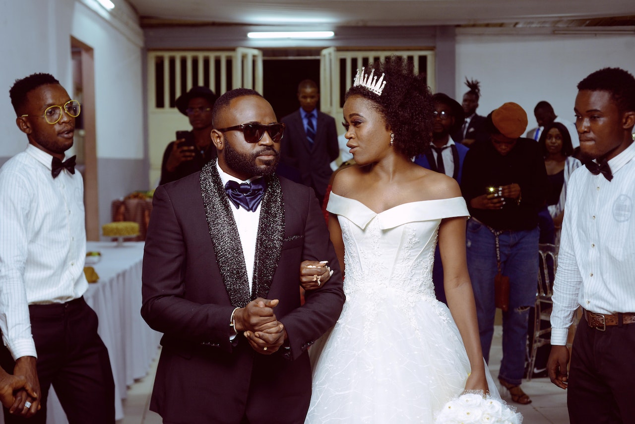 Groom in dark suit and sunglasses walking in with a bride in white dress.