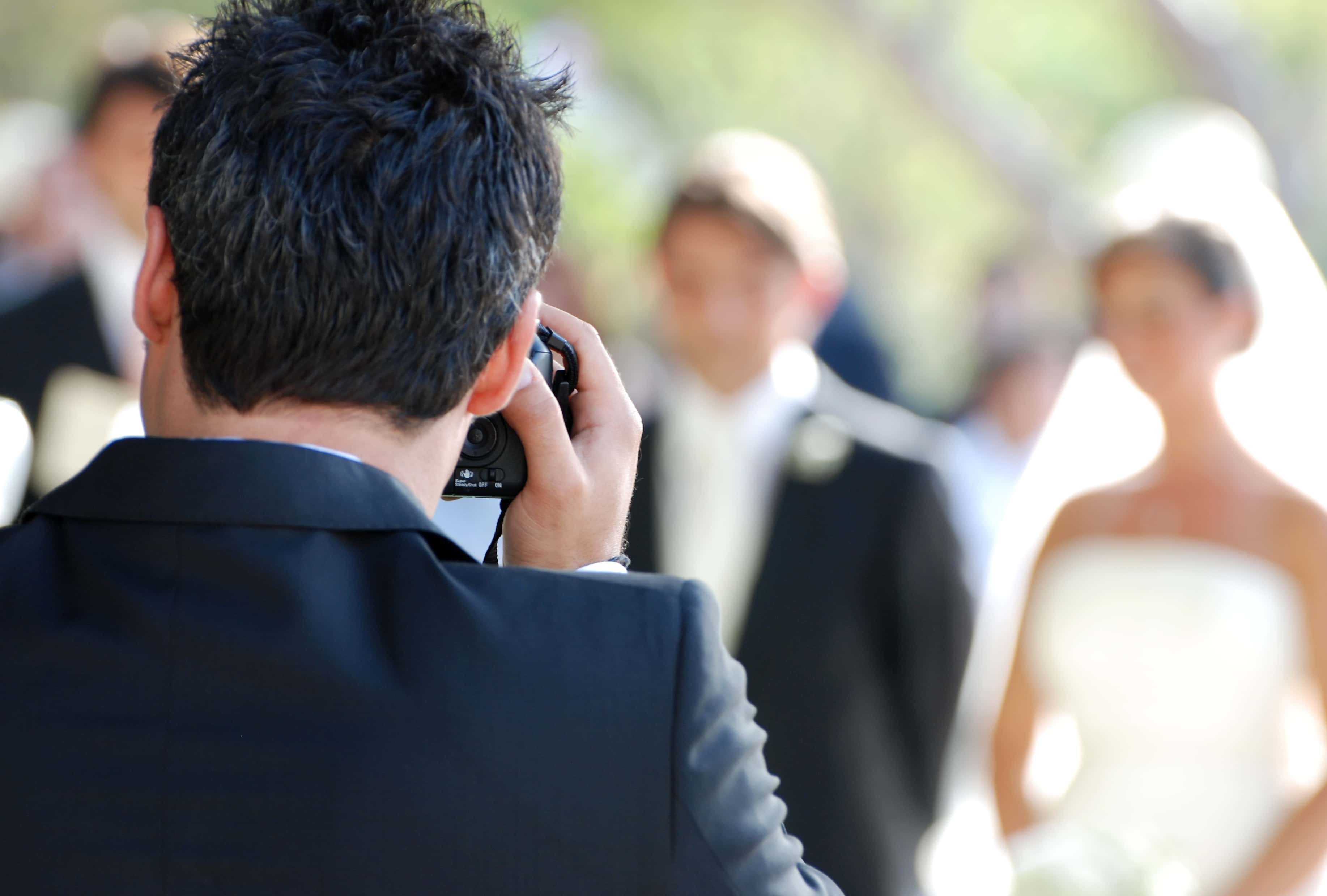 Wedding photographer in black suit taking photos at wedding.