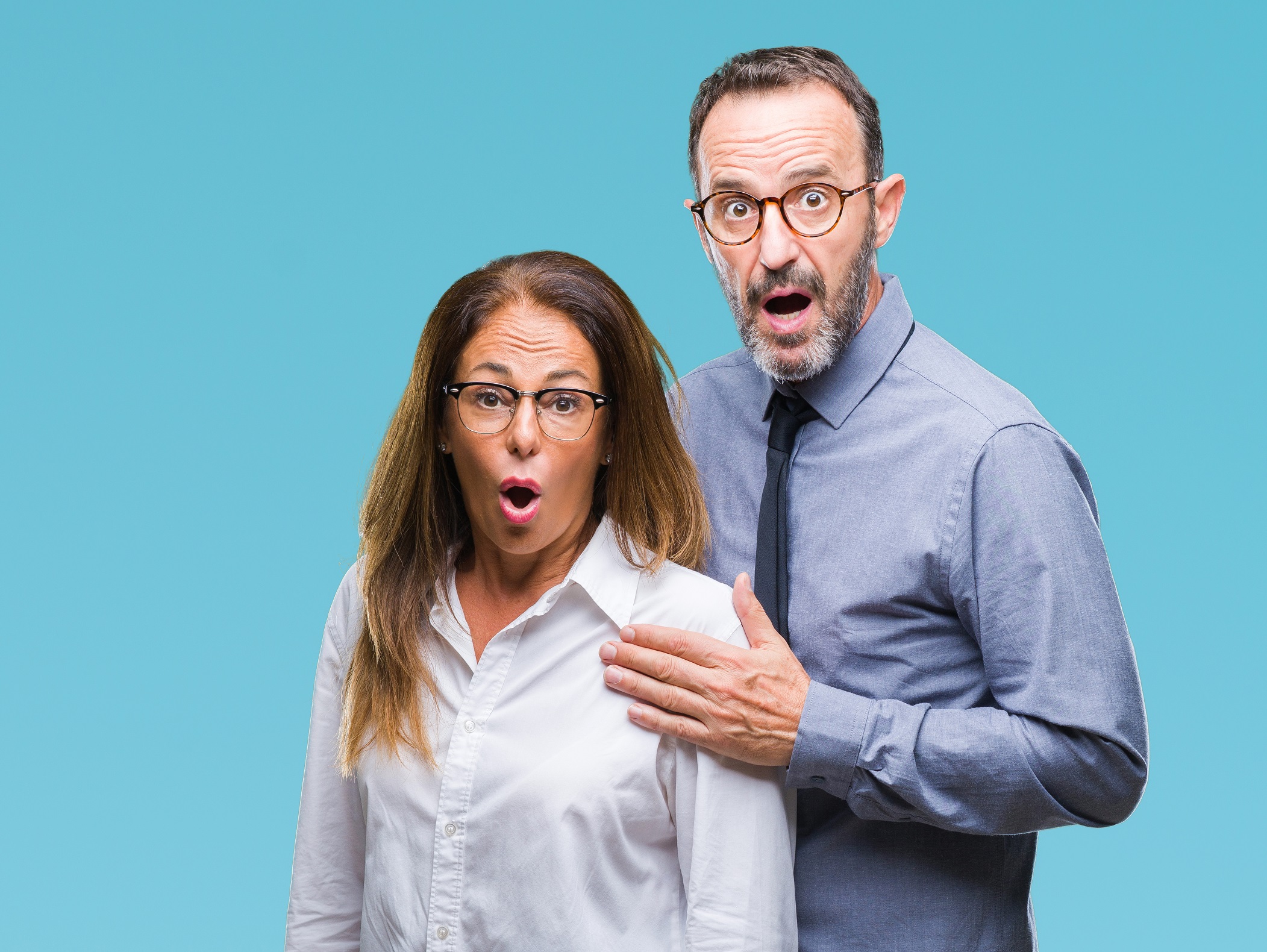 Middle age couple wearing shirts and glasses looking shocked.