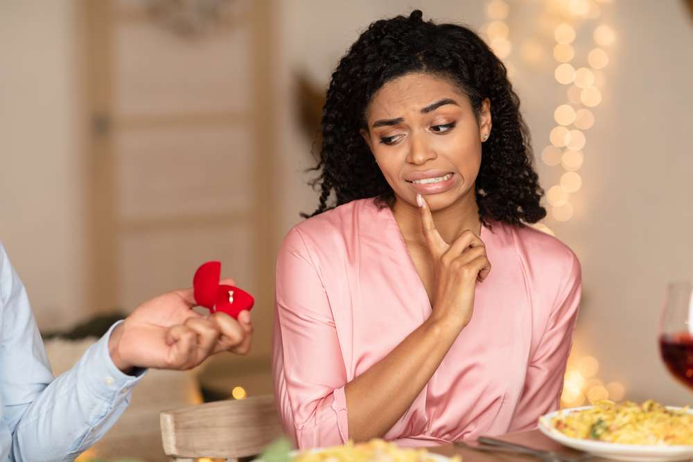 Confused african american woman in doubt looking at engagement ring