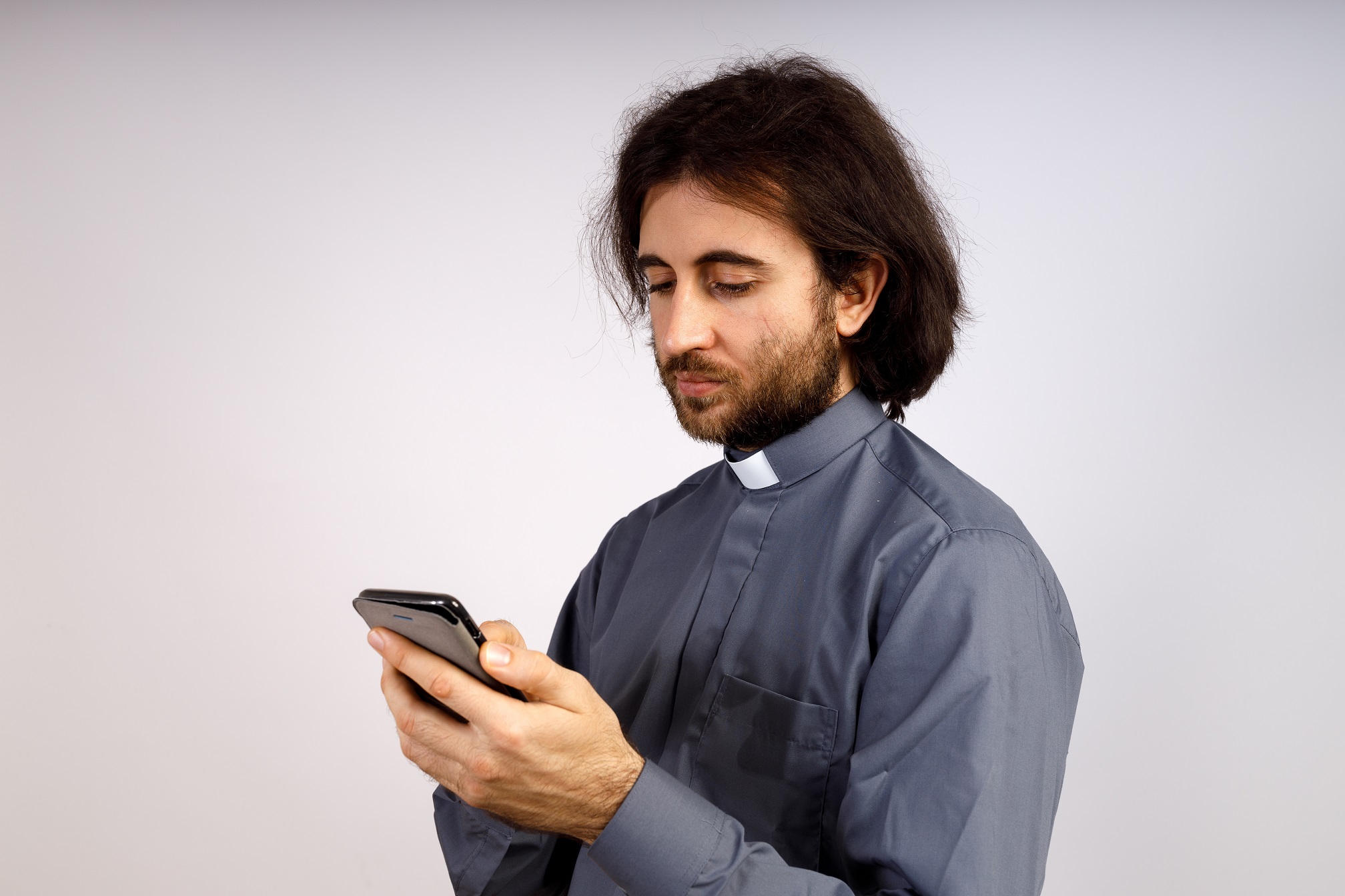 Priest is looking at his phone, looking down.