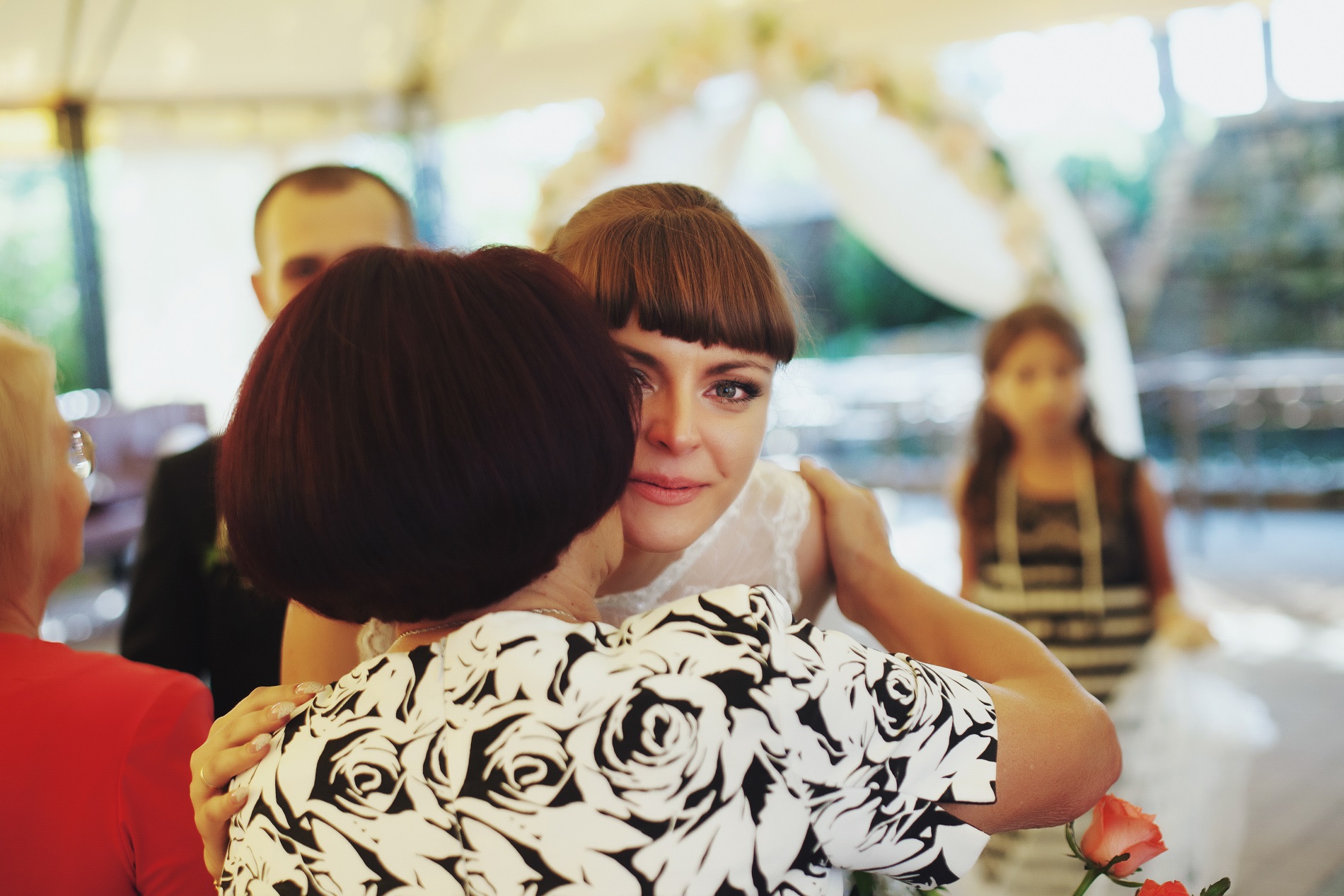 Woman is talking and hugging the bride in white dress at wedding ceremony.