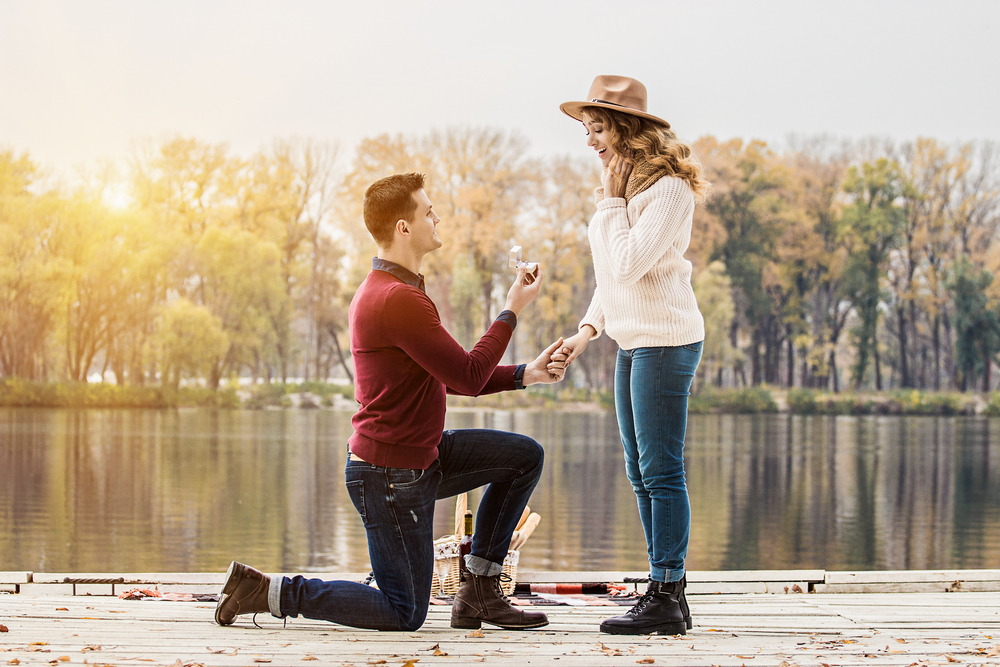 Horizontal shot of young man in casual clothing standing on one knee and holding engagement ring