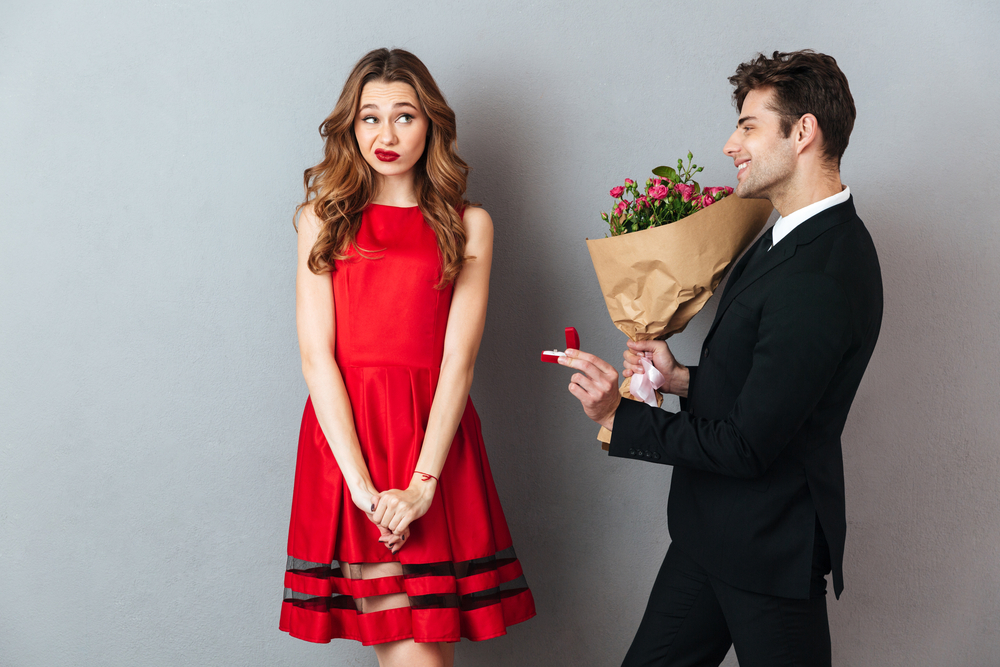 Portrait of a smiling man proposing to a girl with flowers and an engagement ring