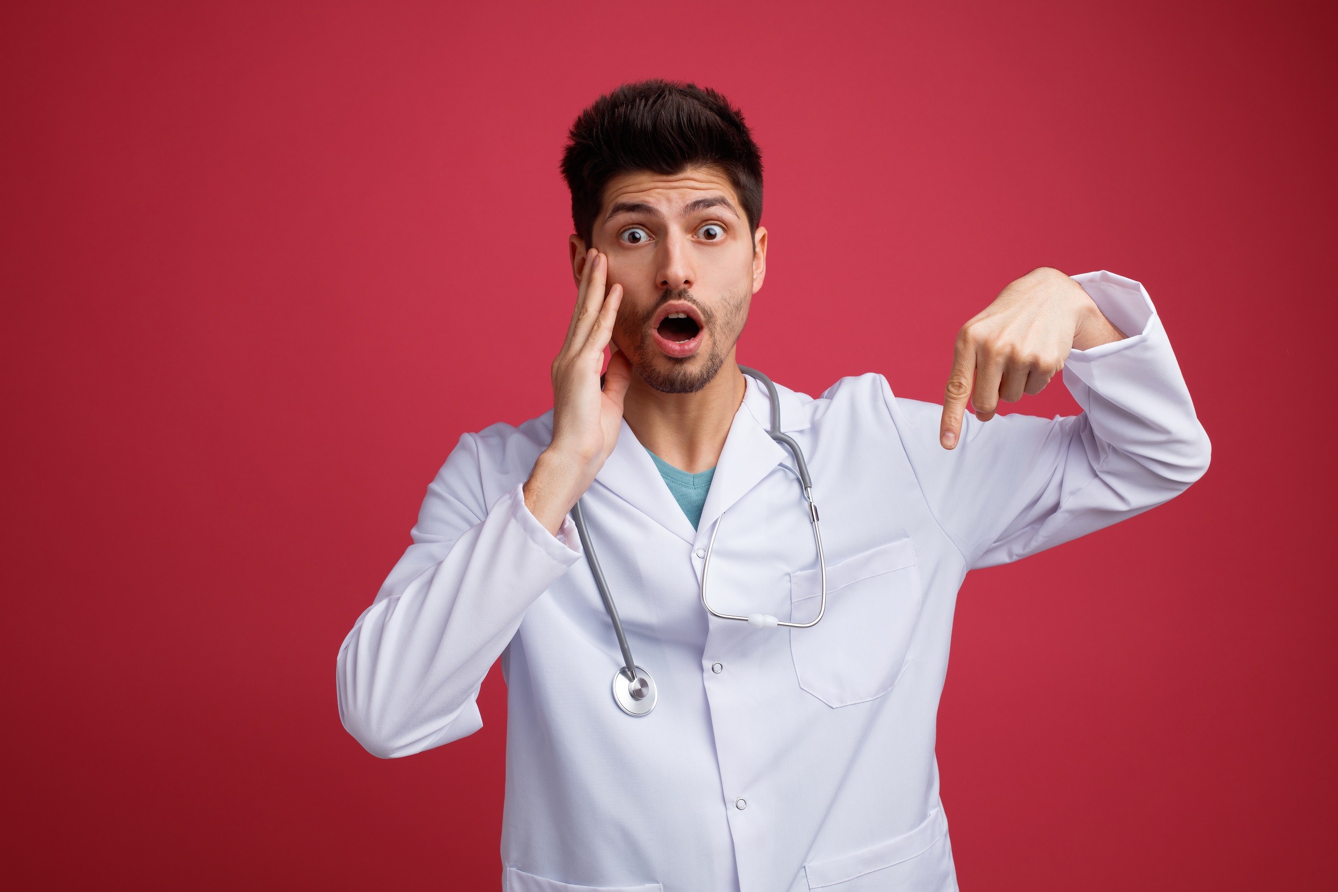 Male doctor wearing medical uniform and stethoscope looking shocked.