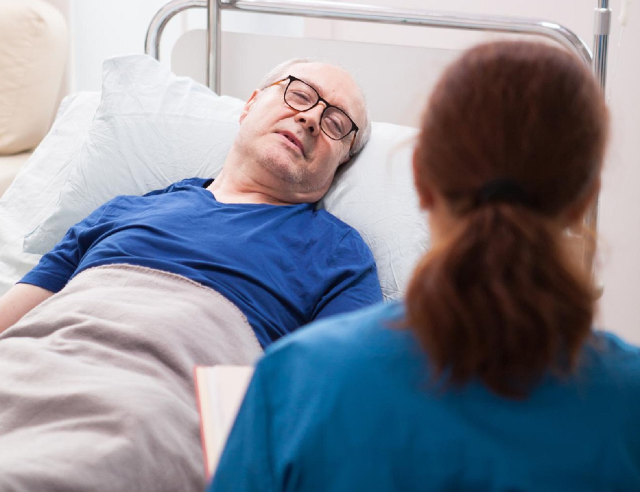 Senior man is laying in hospital bed and talking with a female doctor.