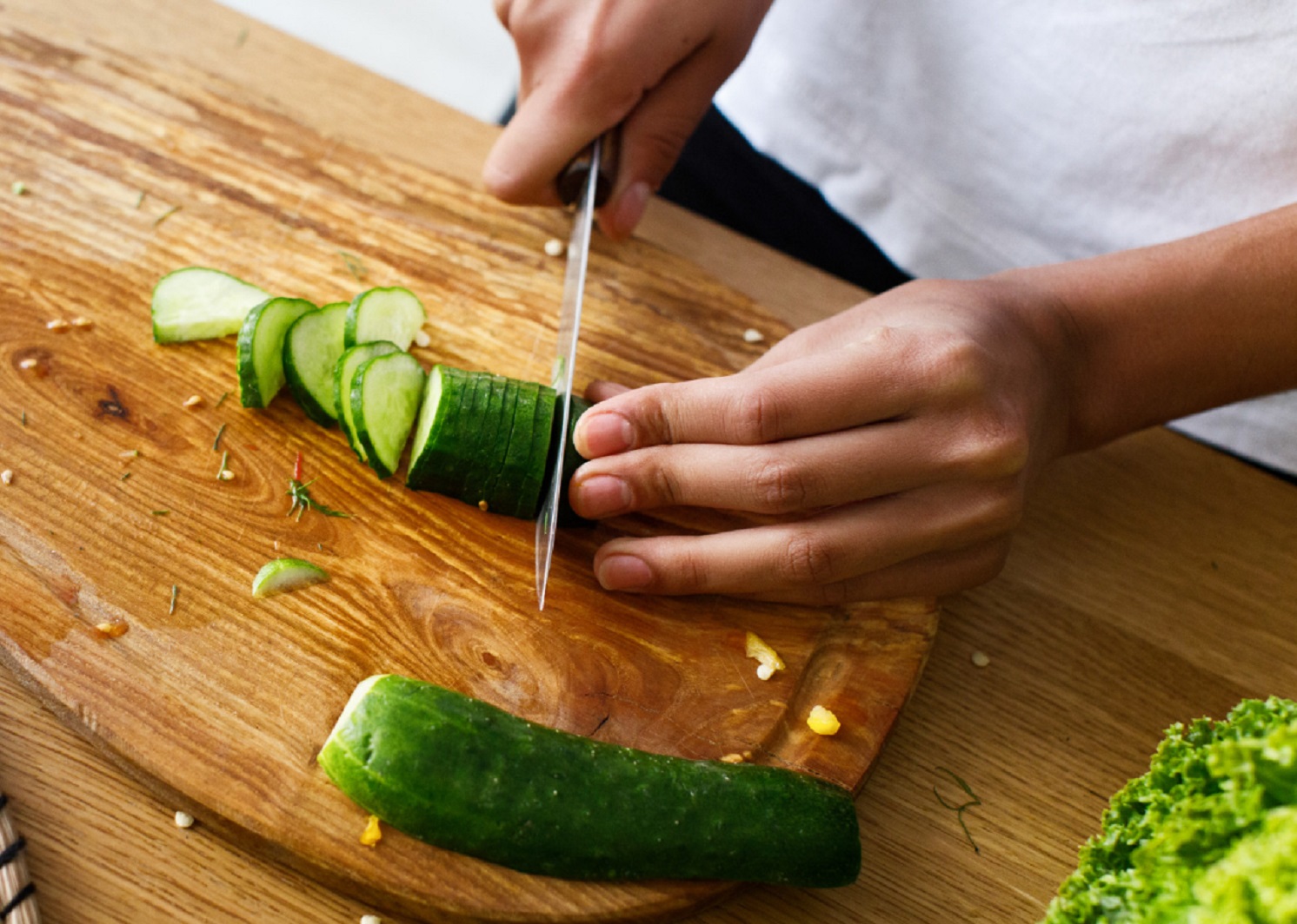 Man is cutting a cucumber on a kitchen desk.
