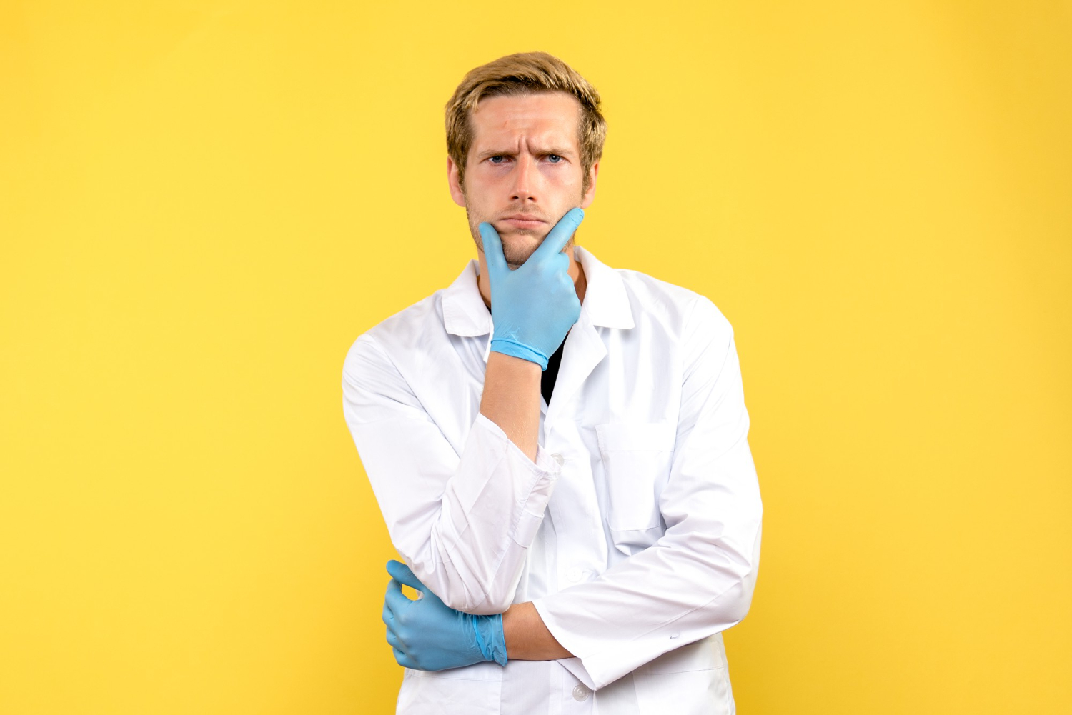 Male doctor thinking, on light yellow background lookin upset.