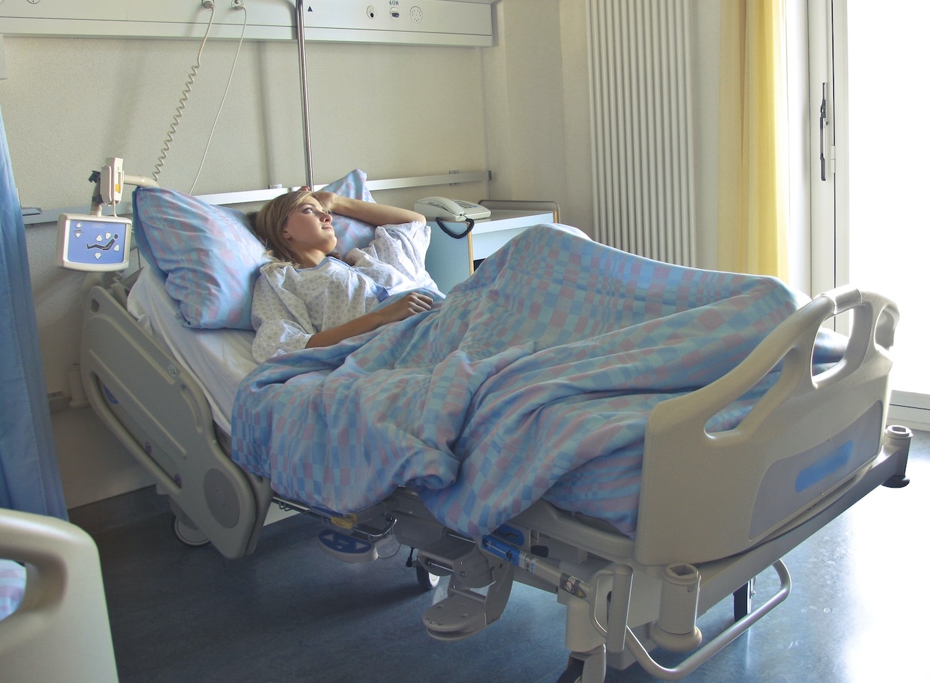 Woman laying in hospital bed in white pajamas.